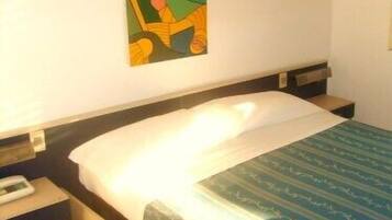 A hotel room with a bed, a nightstand, a wall-mounted painting, and a window.