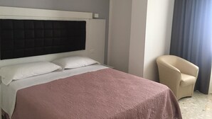 A hotel room with a bed, a chair, and an air conditioning unit.