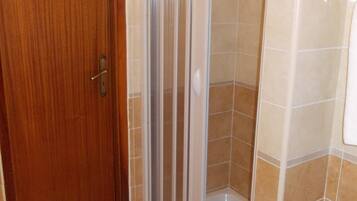 Un baño con puerta de madera, cabina de ducha de vidrio y paredes con azulejos color beige.