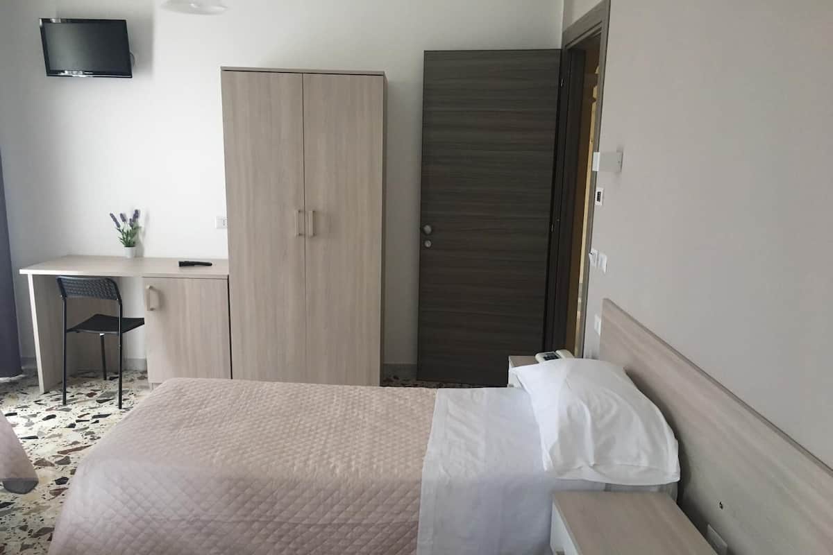 A hotel room with a bed, a desk, a chair, and a wardrobe.