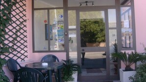 A restaurant with a glass door entrance, outdoor seating with chairs, and potted plants.