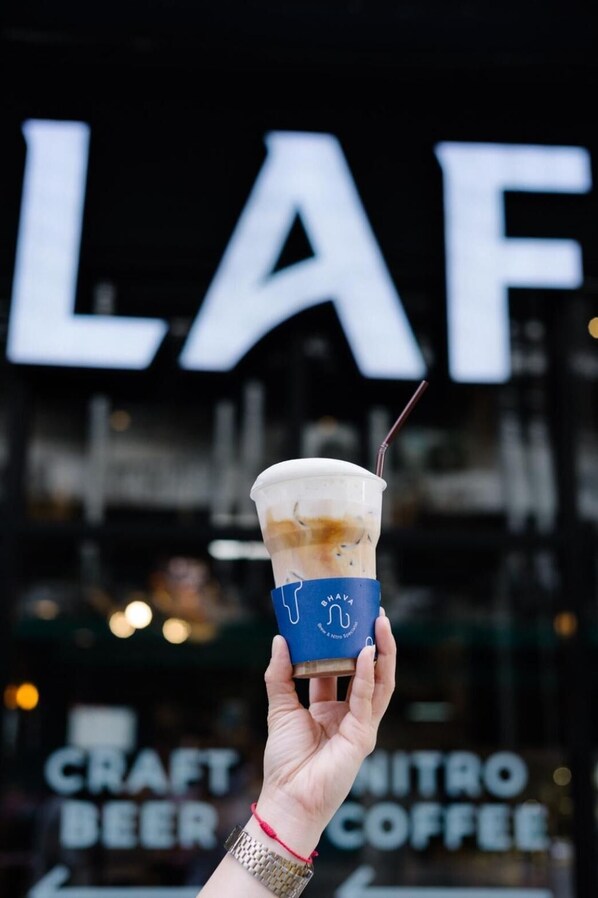A hand holding a cup of iced coffee with a straw, in front of a sign that reads "CRAFT NITRO COFFEE".