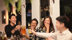 A group of people toasting with drinks at a bar with bottles and glasses on the counter.