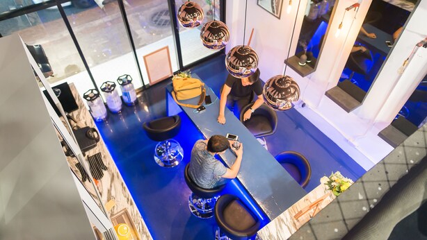 A modern bar area with a blue floor, black bar stools, and hanging spherical light fixtures.