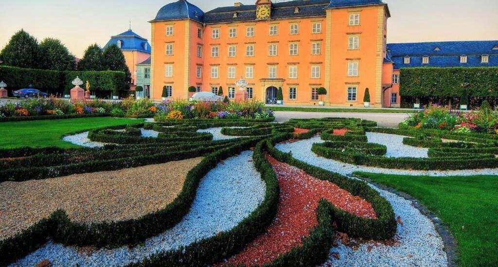 A large hotel with a symmetrical garden featuring geometric patterns and a central pathway.