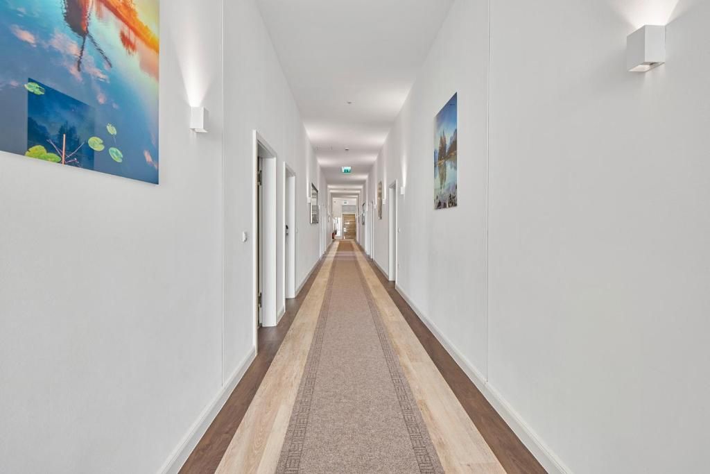 A hotel hallway with a carpeted floor, white walls, and artwork on the walls.
