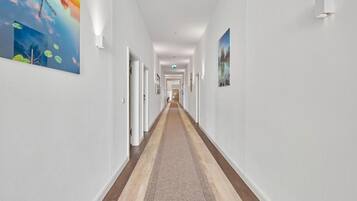 A hotel hallway with a carpeted floor, white walls, and artwork on the walls.