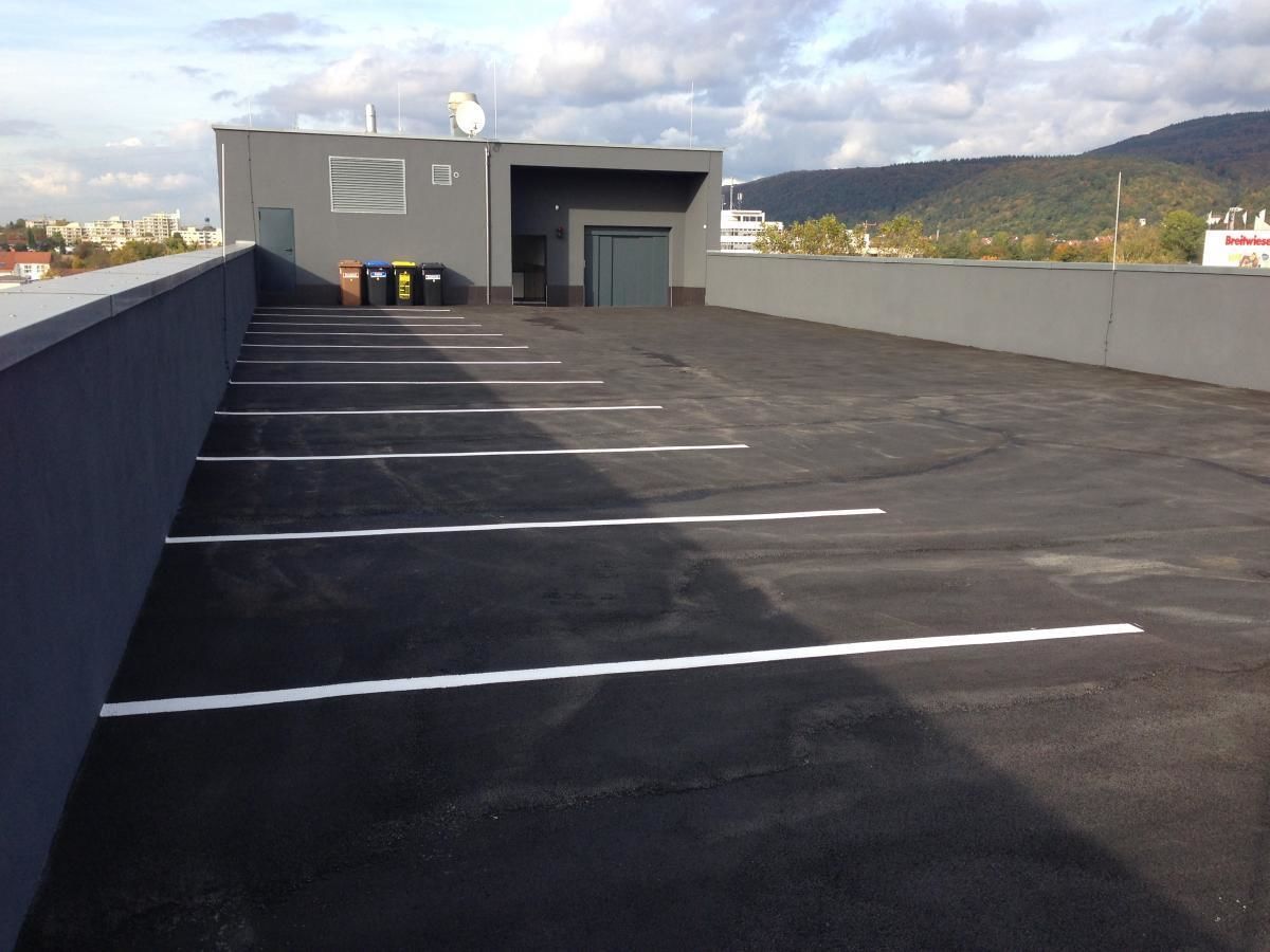A rooftop parking area with marked spaces, a building entrance, and a view of a cityscape and mountains in the background.