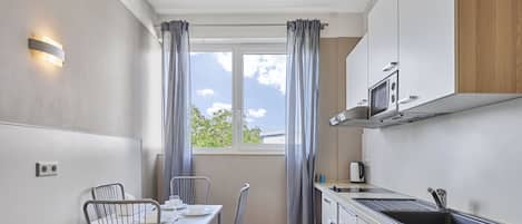 A compact kitchen with a dining area, a window with curtains, and a microwave.