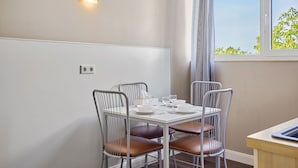 A dining area with a white table, four metal chairs, and a window with a view of greenery. - Boardinghotel Heidelberg (Heidelberg)