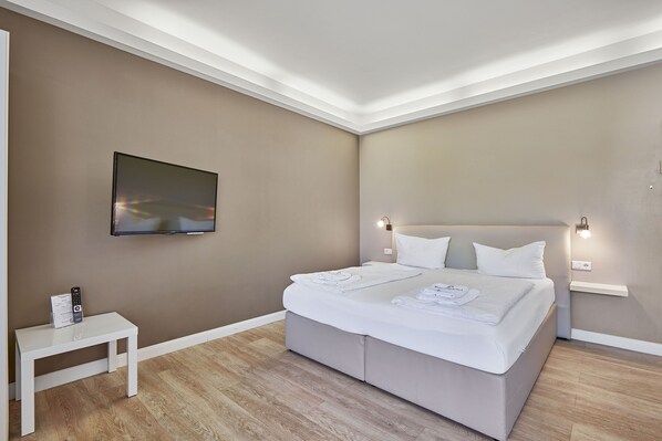 Une chambre moderne avec un grand lit, des lampes de chevet, une petite table et un téléviseur fixé au mur.