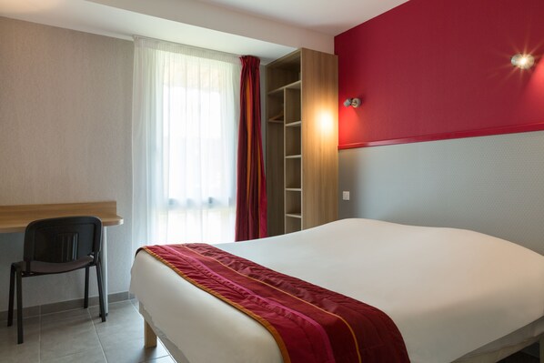Una habitación de hotel con cama, una silla, un armario y una ventana con cortinas.