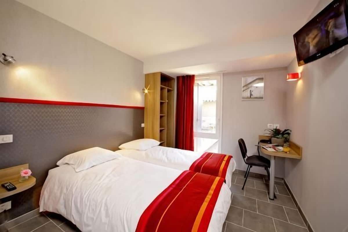 Una habitación de hotel con dos camas, un escritorio, una silla, una mesita de noche y un televisor.