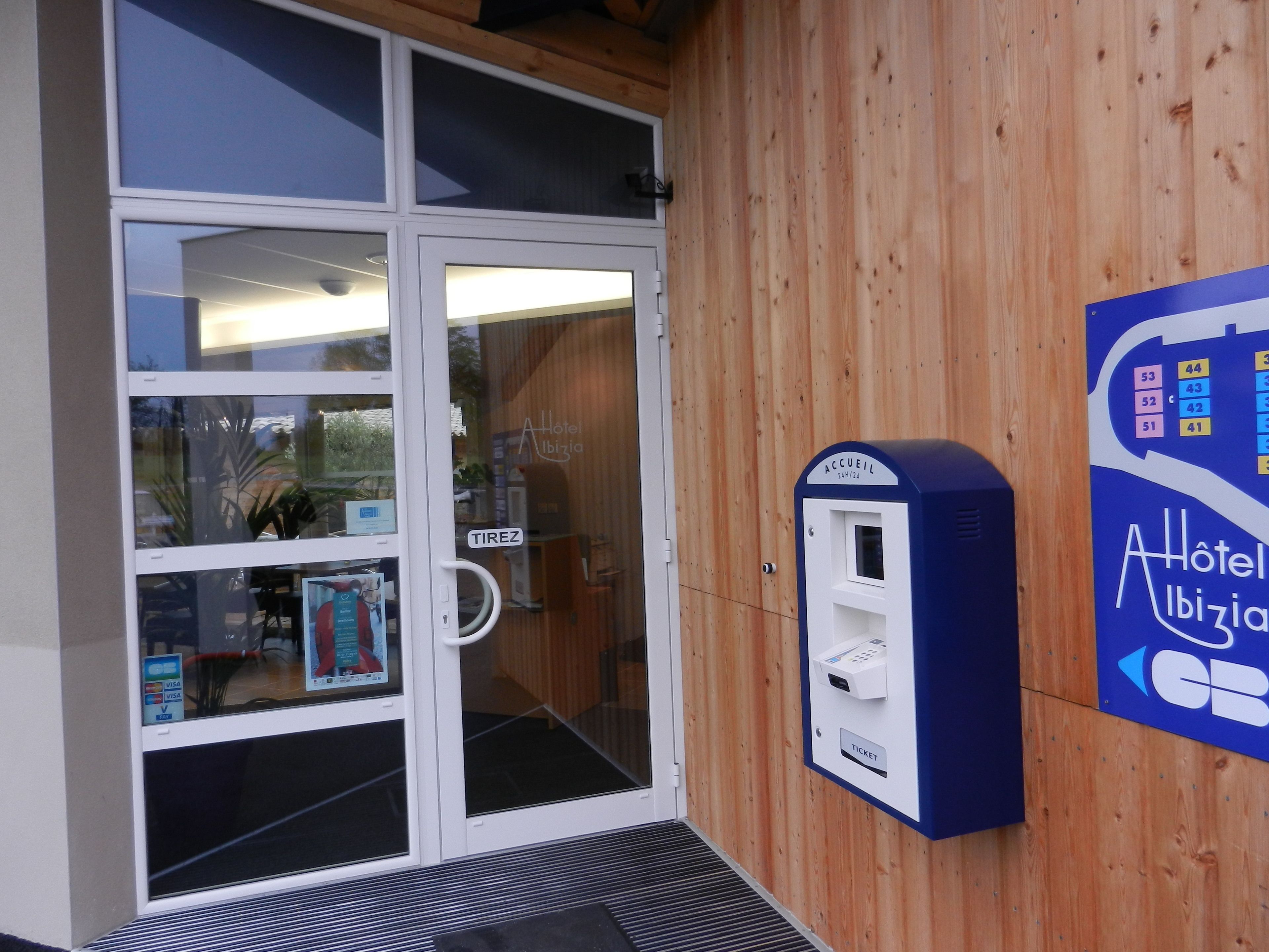 A hotel entrance with a glass door, a wooden wall, and a ticket machine.