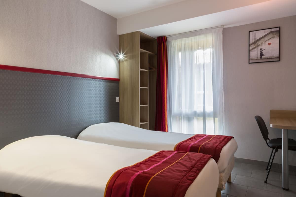 Habitación de hotel con dos camas, un escritorio, una silla, un armario y una ventana con cortinas.