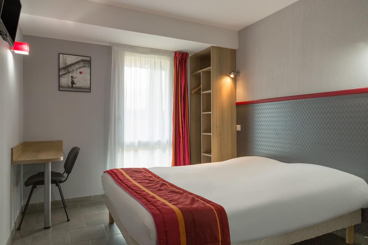 Habitación de hotel con cama, escritorio, silla, armario y ventana con cortinas.