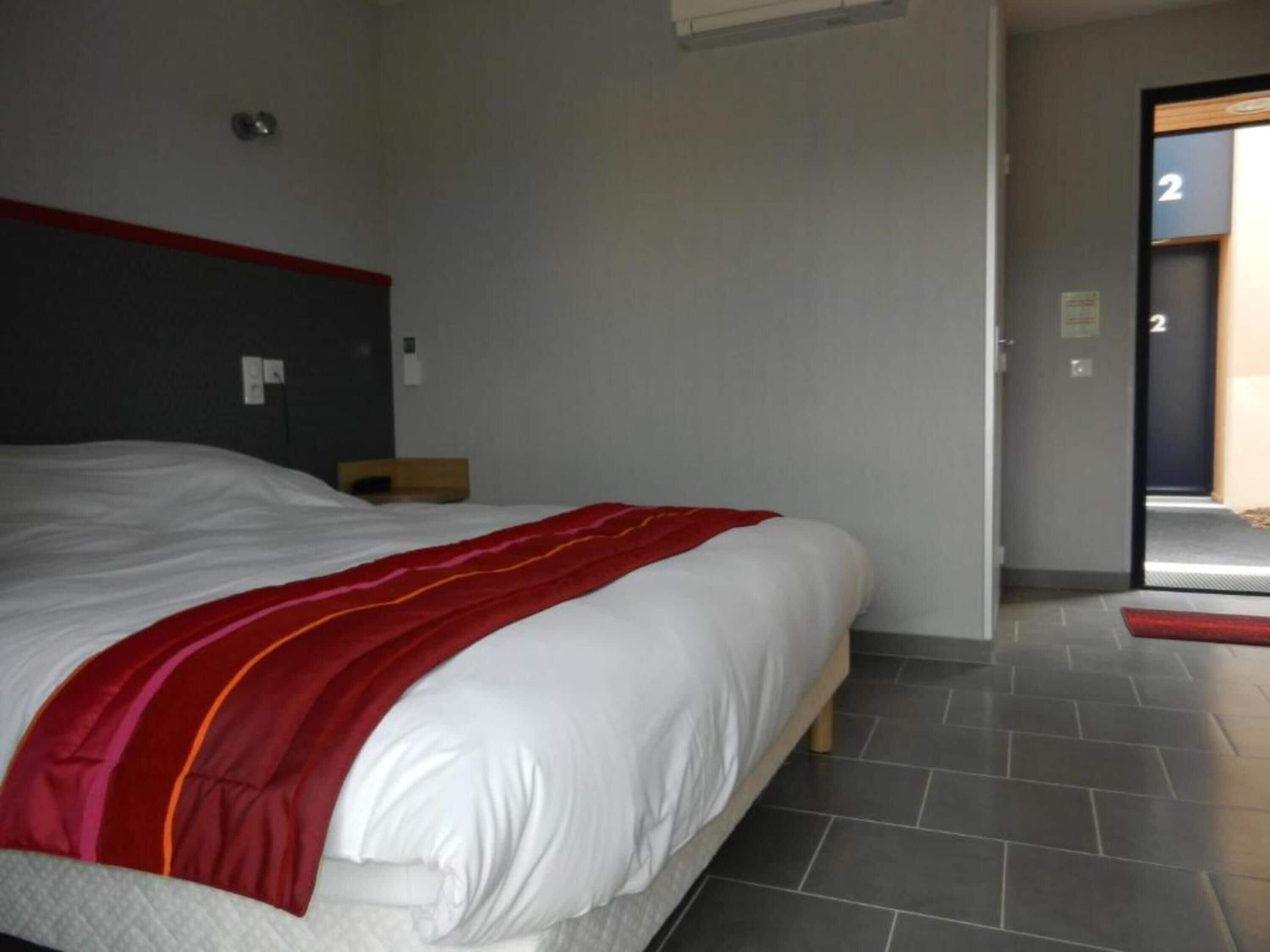 A hotel room with a large bed, a red and white striped blanket, a wooden headboard, and a tiled floor.