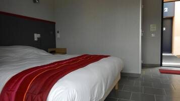 A hotel room with a large bed, a red and white striped blanket, a wooden headboard, and a tiled floor.