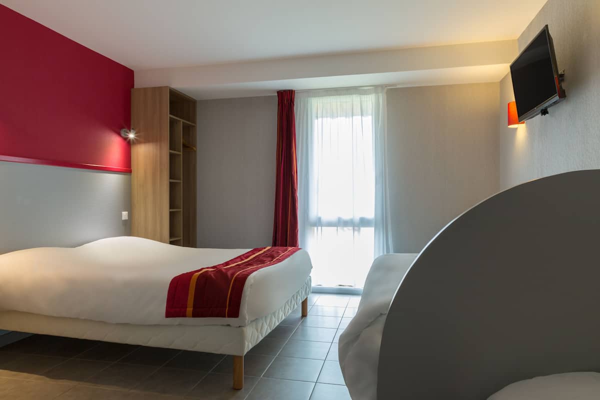 Una habitación de hotel con una cama, una zona de estar, un televisor montado en la pared y un ventanal con cortinas.