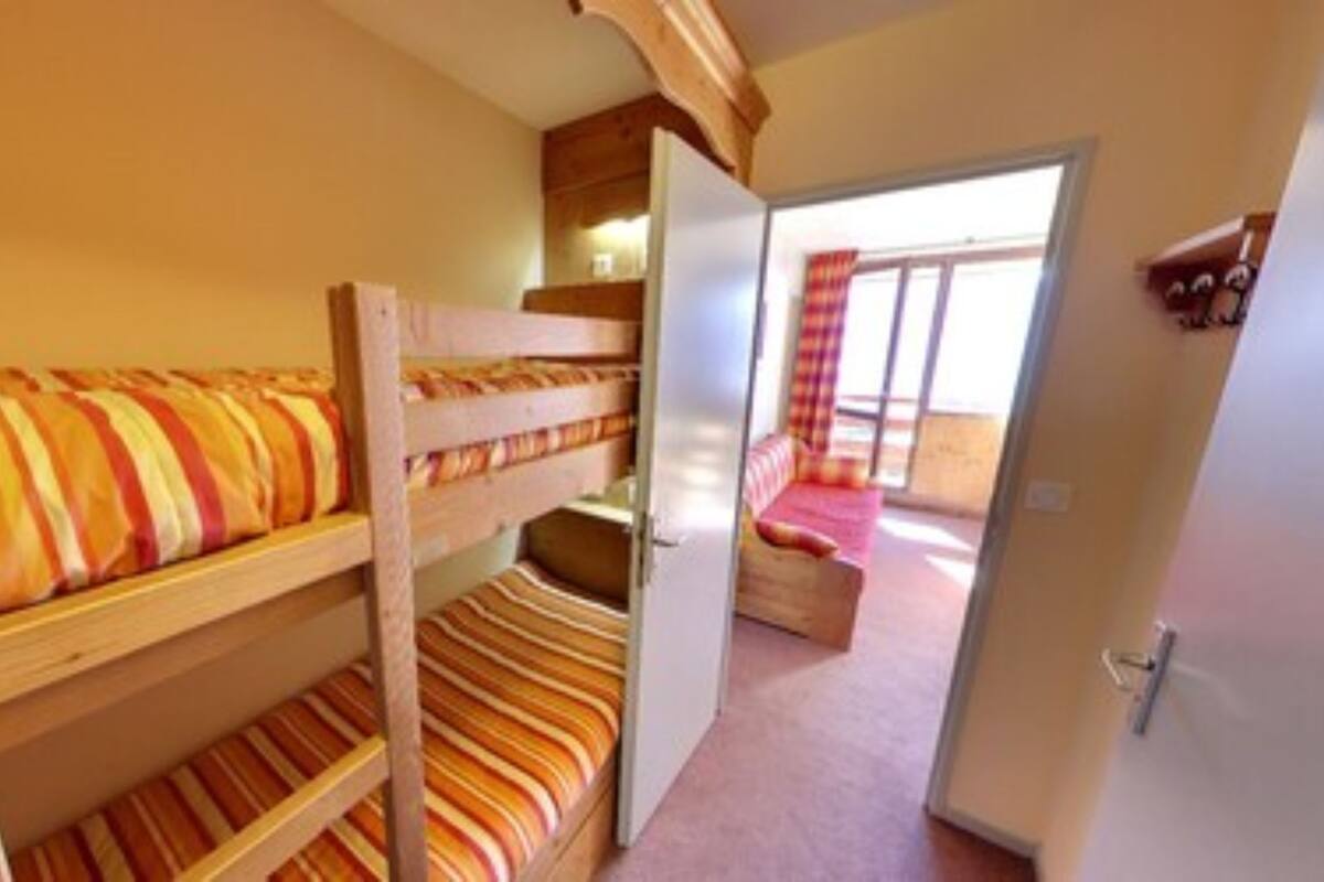 A bunk bed room with striped bedding, a door leading to a balcony, and a small wooden cabinet.