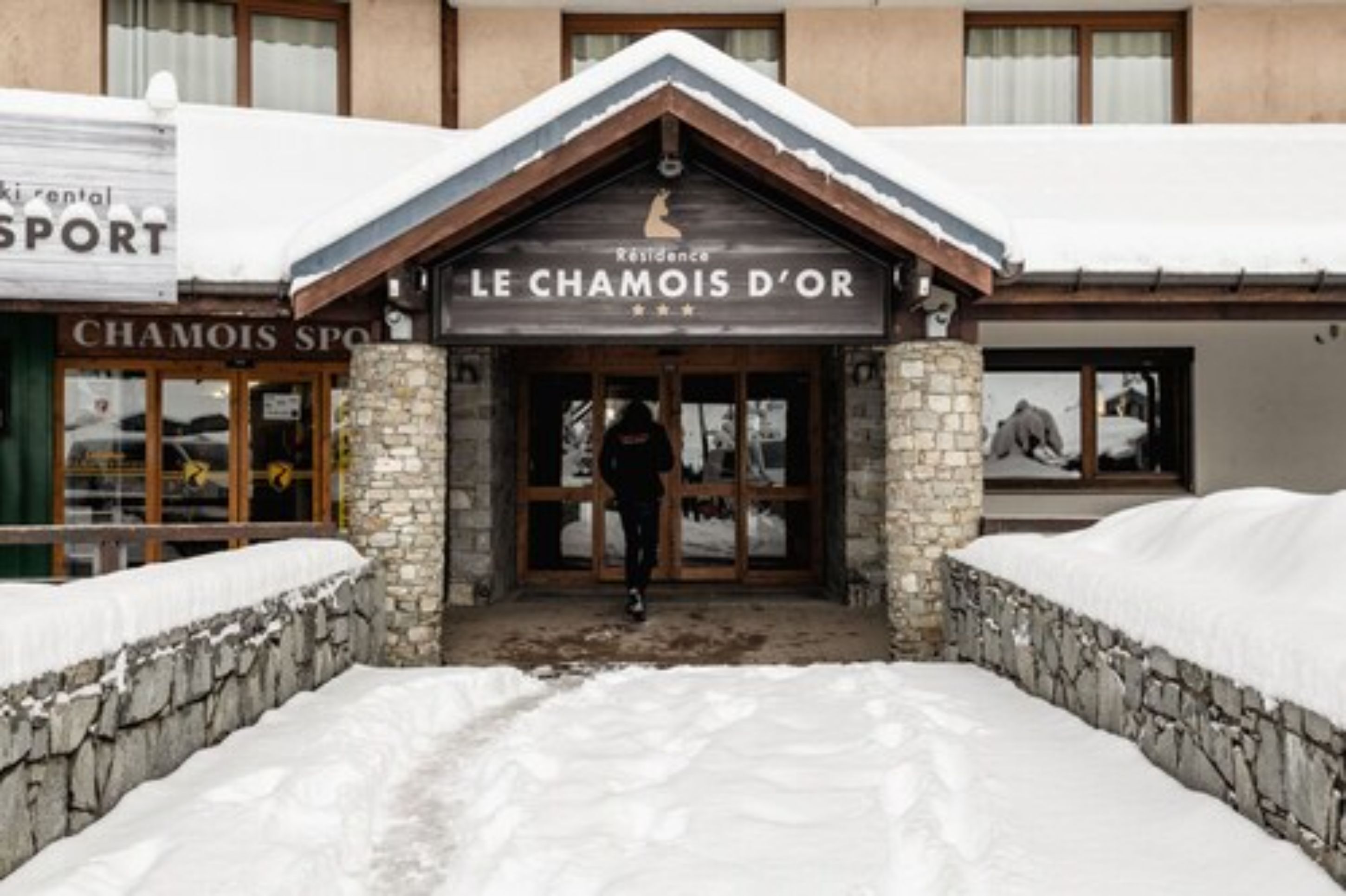 A hotel entrance with a stone facade and a wooden roof, surrounded by snow.