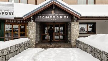 A hotel entrance with a stone facade and a wooden roof, surrounded by snow.
