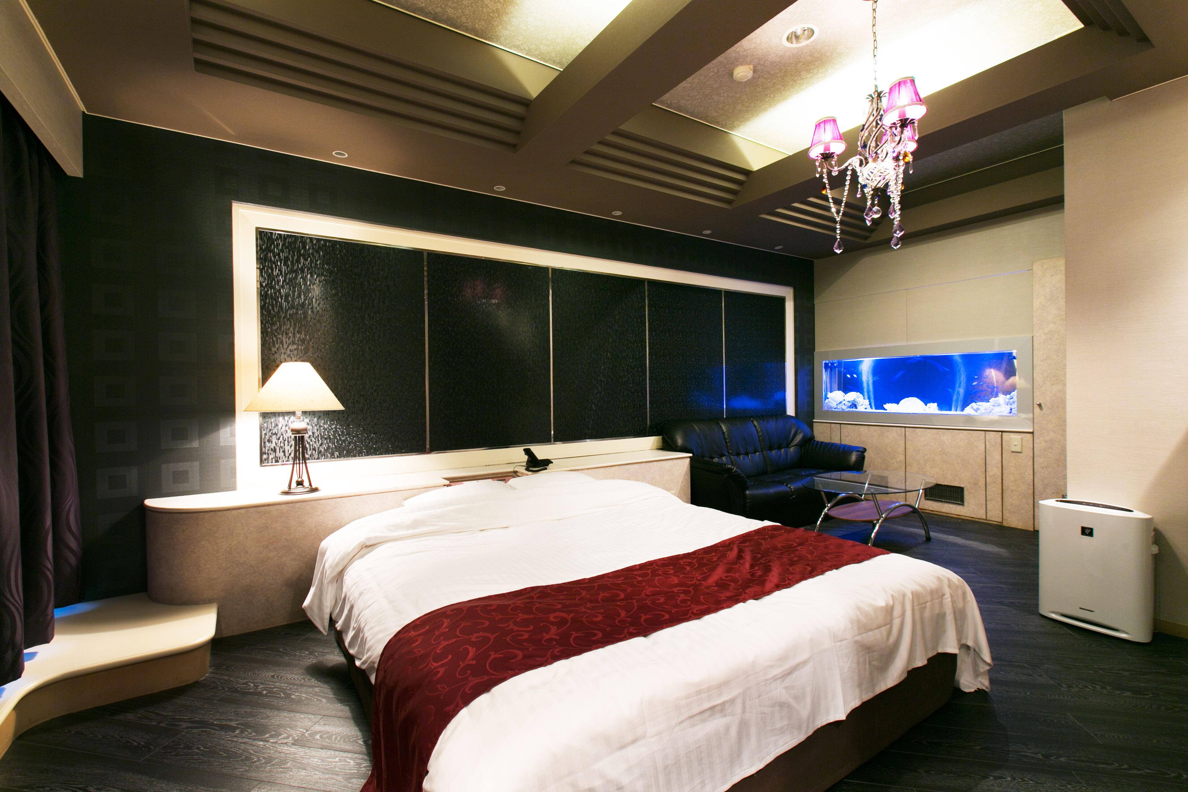 Une chambre d’hôtel moderne avec un grand lit, un coin salon avec un fauteuil, une télévision et une grande fenêtre.