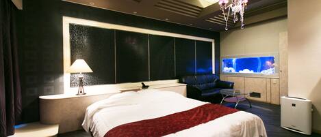 Une chambre d’hôtel moderne avec un grand lit, un coin salon avec un fauteuil, une télévision et une grande fenêtre.