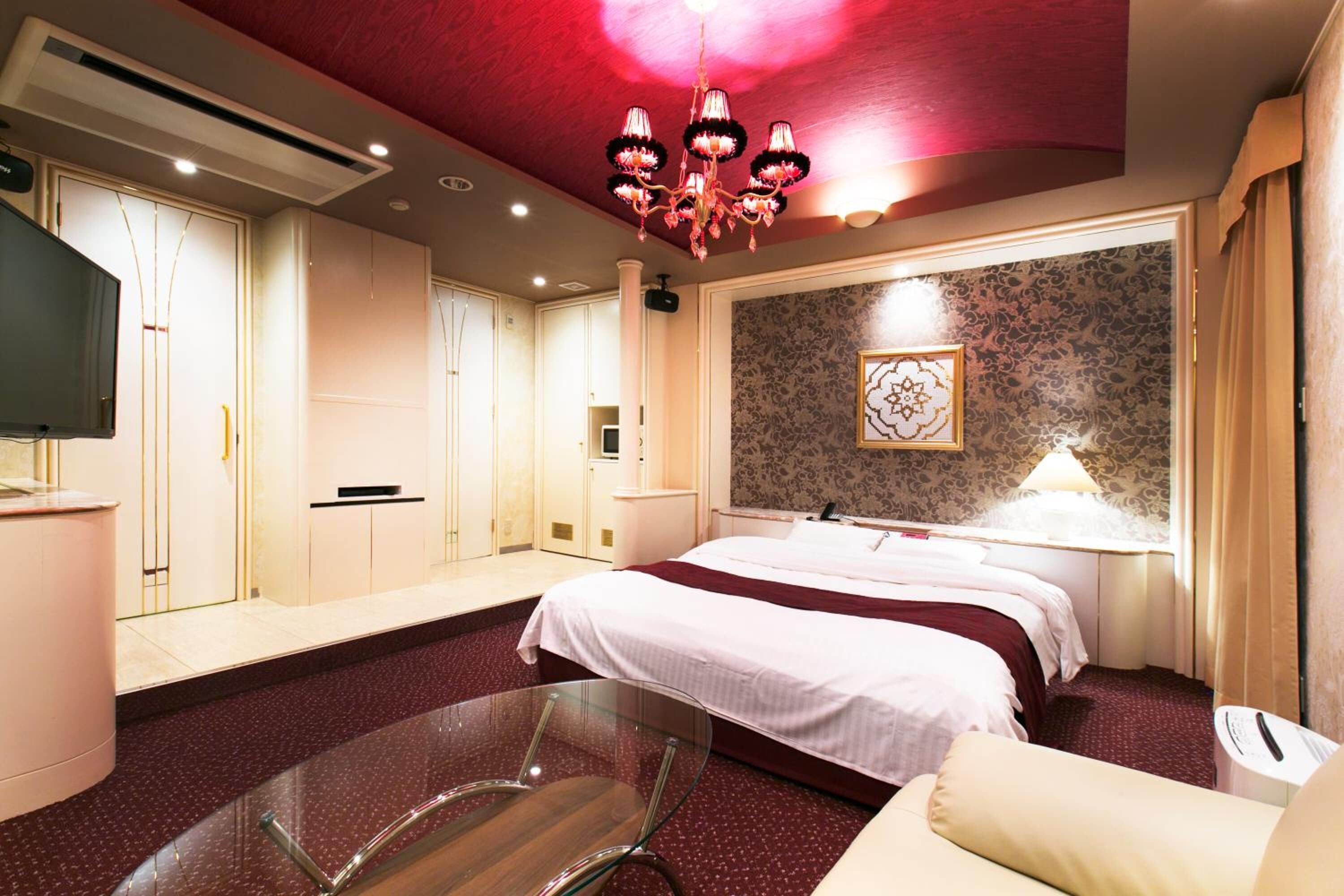 Une chambre d’hôtel avec un grand lit, une table en verre, un téléviseur et un lustre.