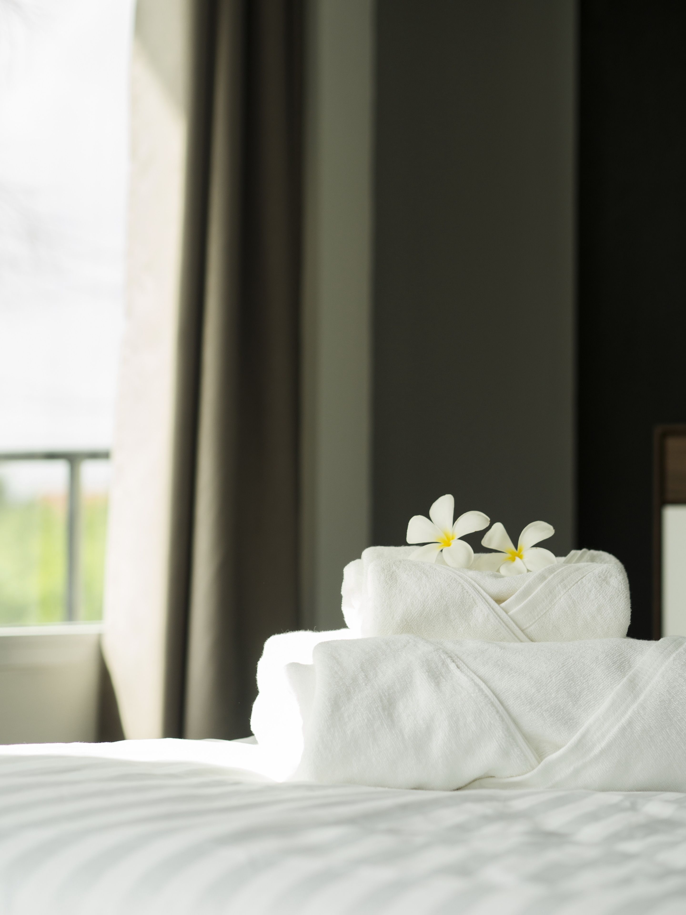 Een net opgemaakt bed met witte lakens en twee witte handdoeken er bovenop, plus een witte bloem.