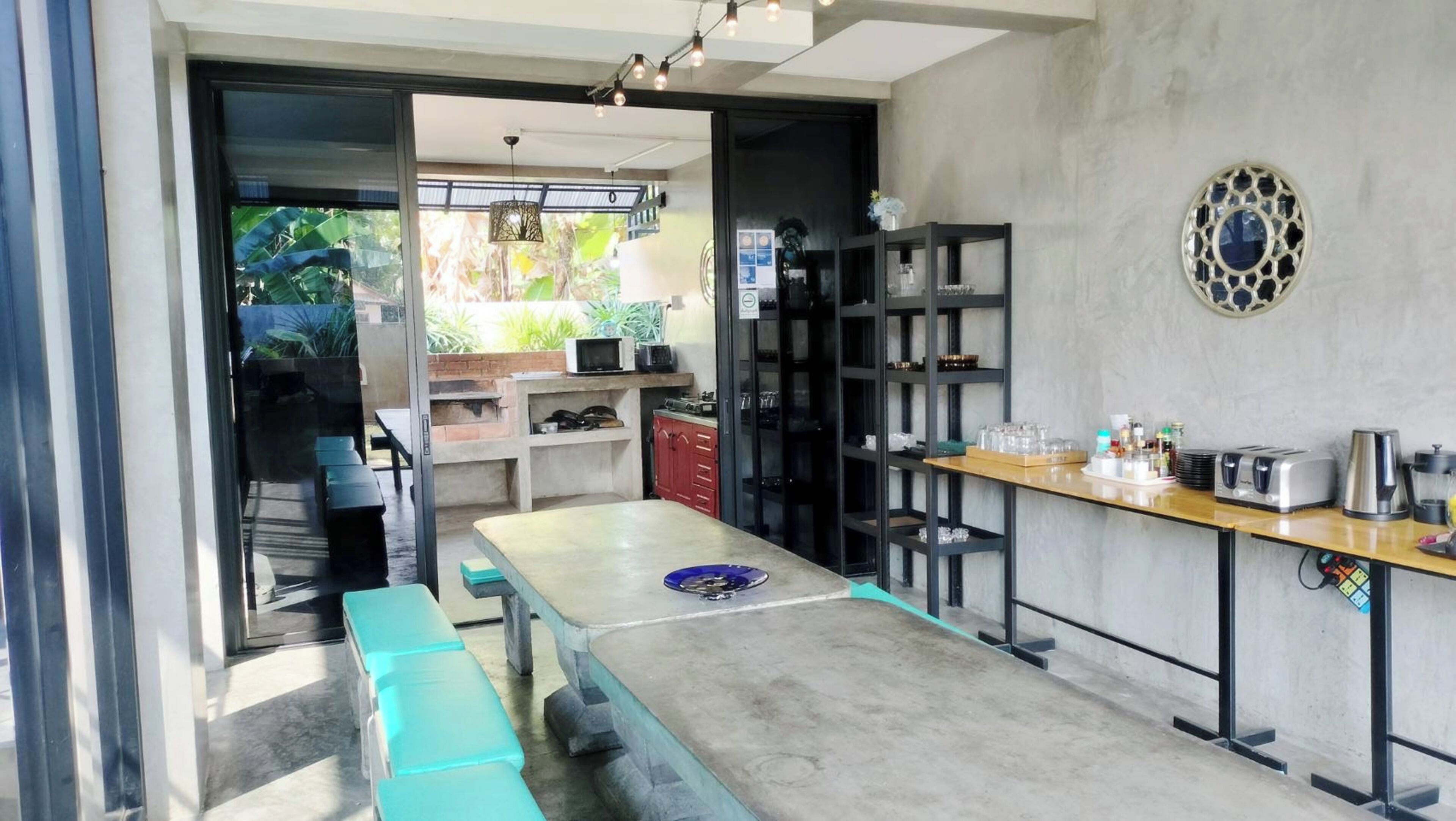 A modern kitchen with a large island, bar stools, and a dining table. There is a view of a garden through the glass door.