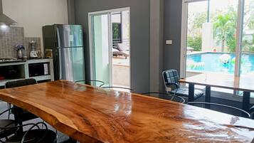A kitchen with a large wooden table, a refrigerator, and a view of a swimming pool.