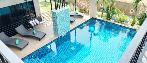 A swimming pool with tiled blue edges, surrounded by lounge chairs and a tiled wall.