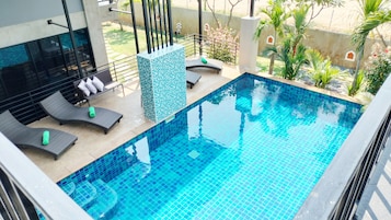 Una piscina con bordes azules de azulejos, rodeada de sillas de descanso y una pared de azulejos.
