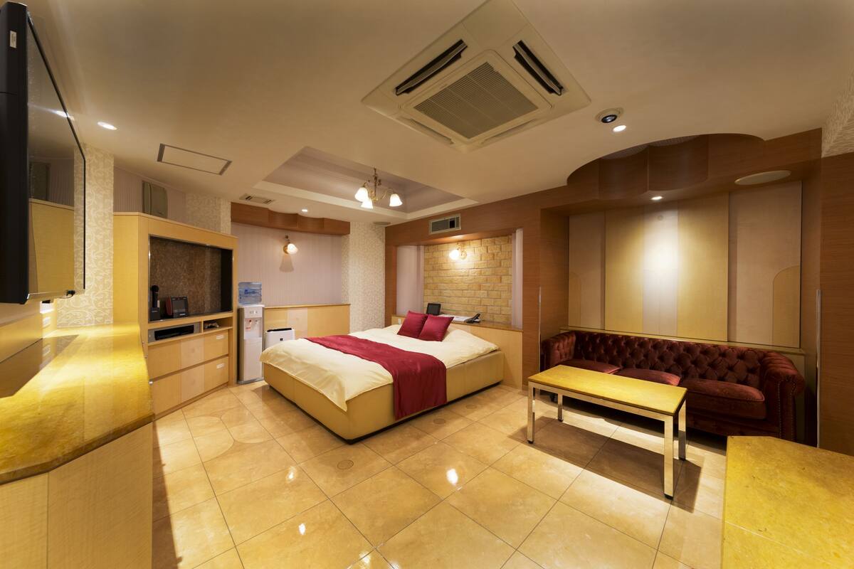 A modern hotel room with a large bed, a sofa, a small table, and a TV.