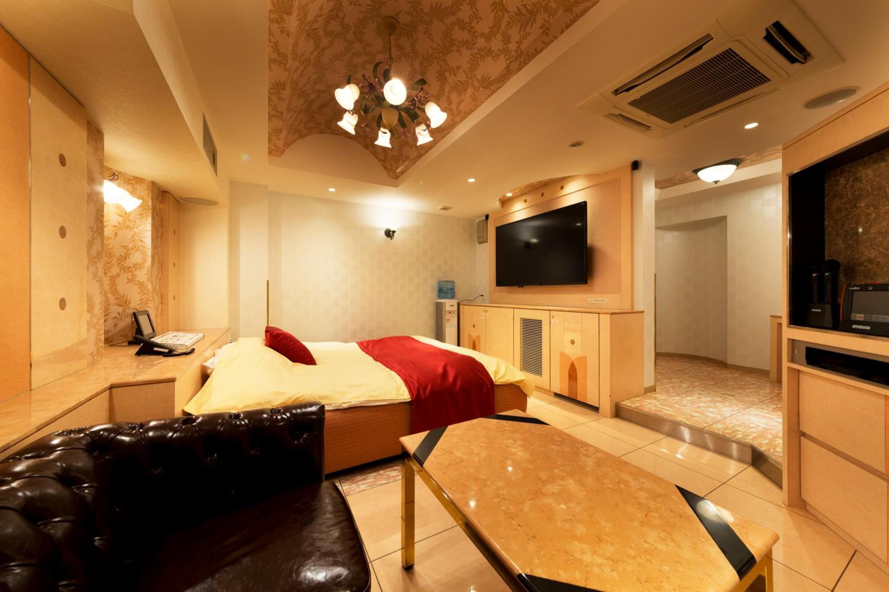 Una habitación de hotel con cama, televisor, sofá, mesa y minibar.