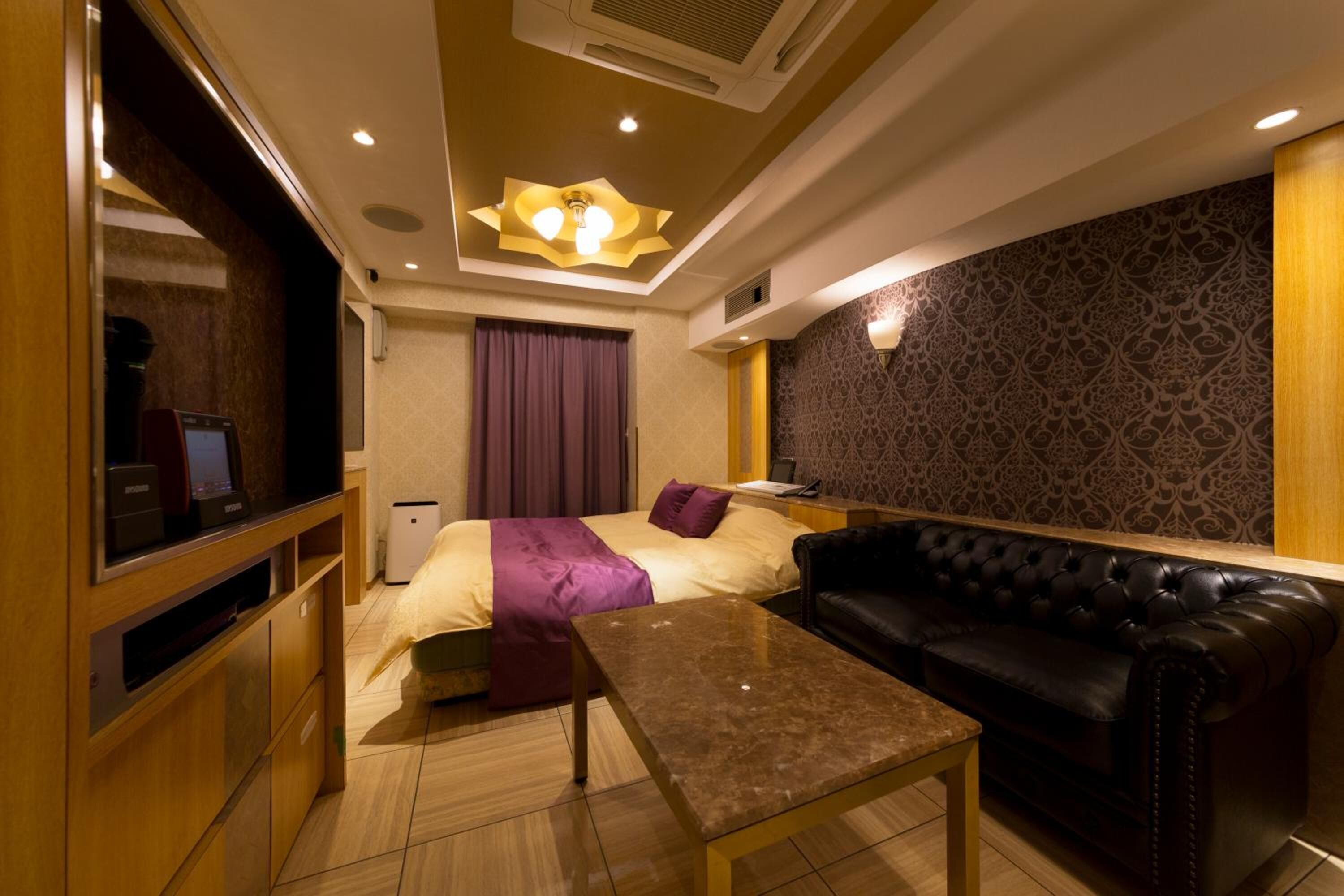 Habitación de hotel con cama, sofá de cuero, una mesita, televisor y pared con diseño.