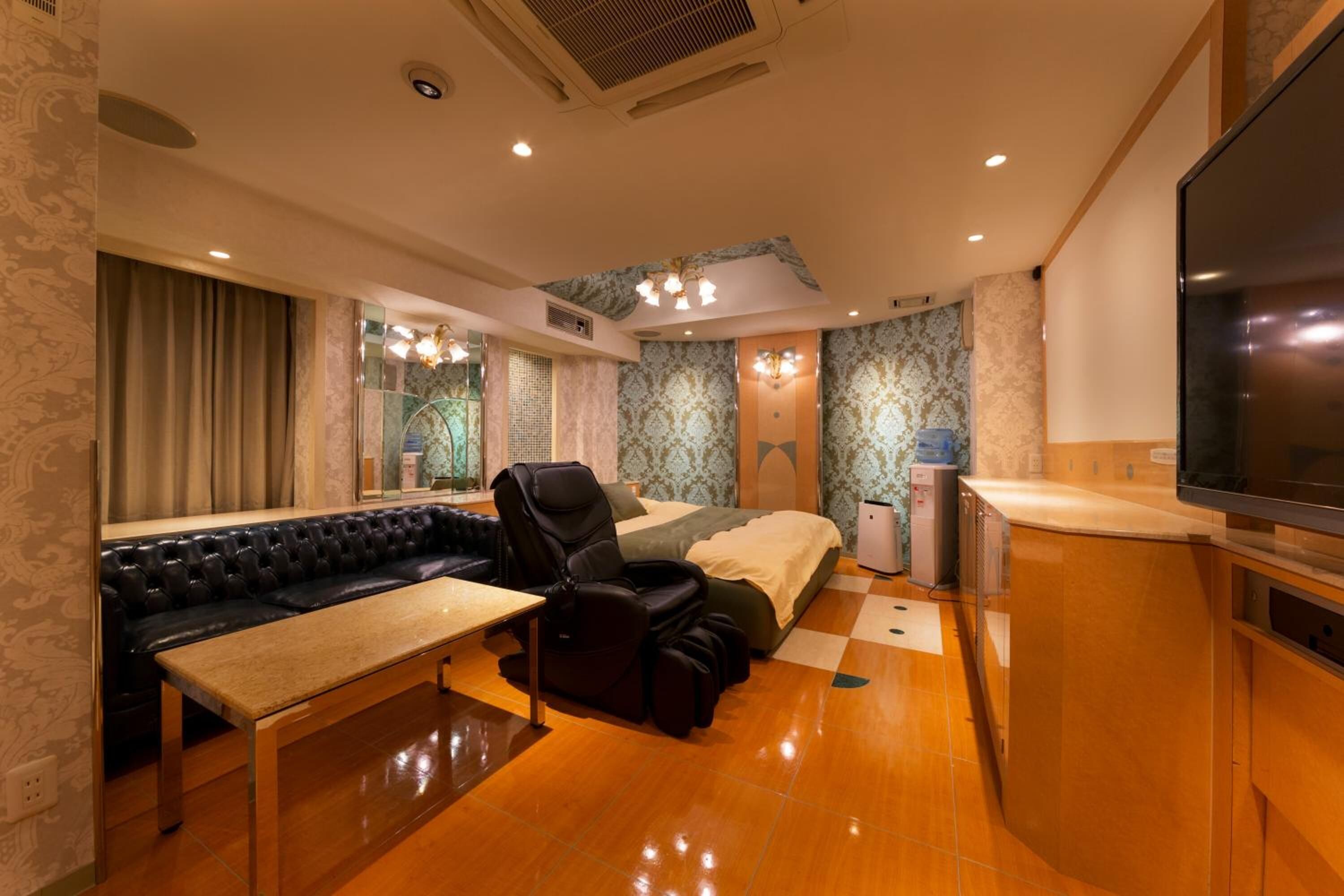 A hotel room with a sofa, massage chair, bed, TV, and a small table.