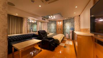 A hotel room with a sofa, massage chair, bed, TV, and a small table.