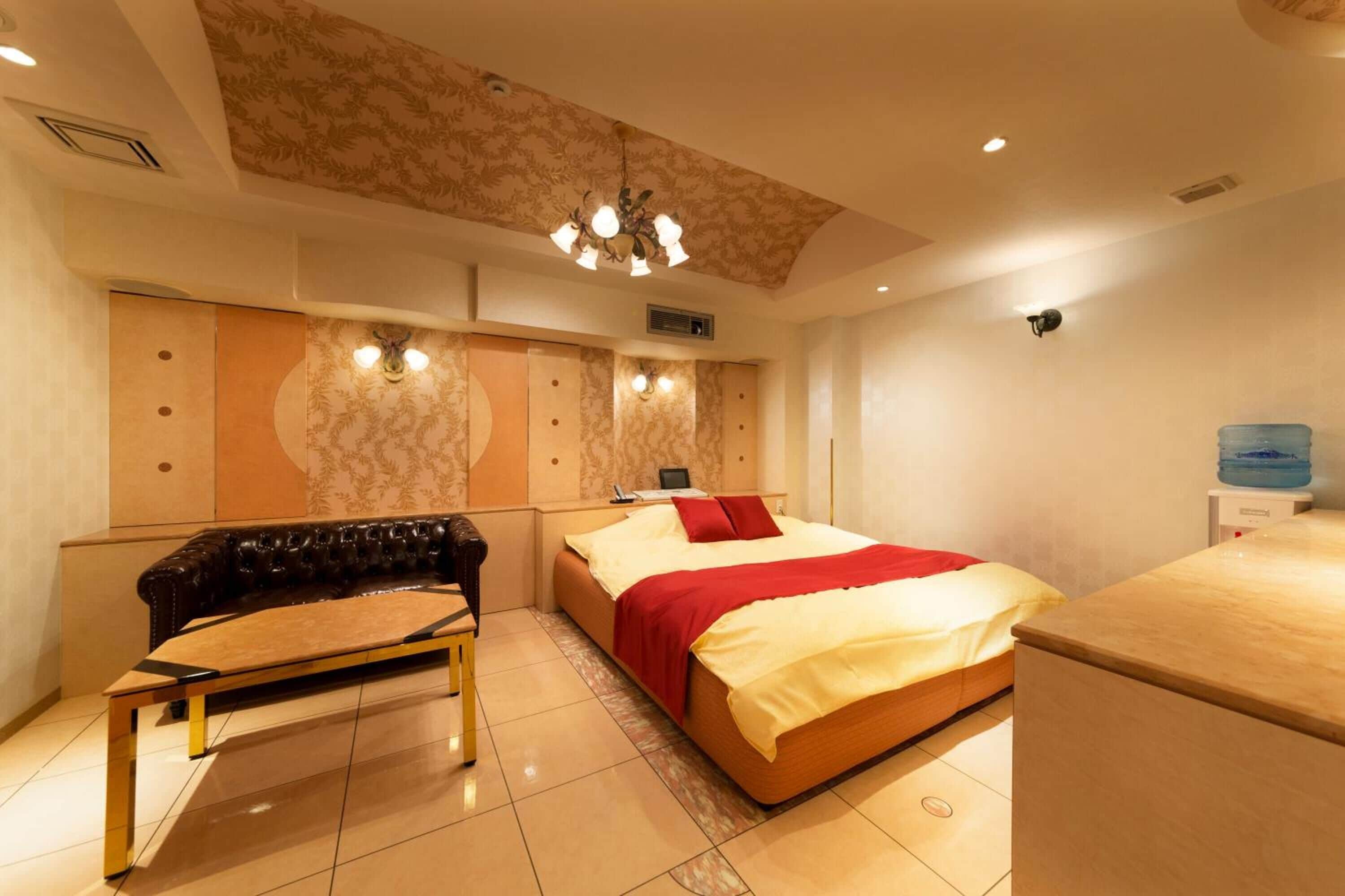 A hotel room with a bed, a sofa, a desk, and a water dispenser.