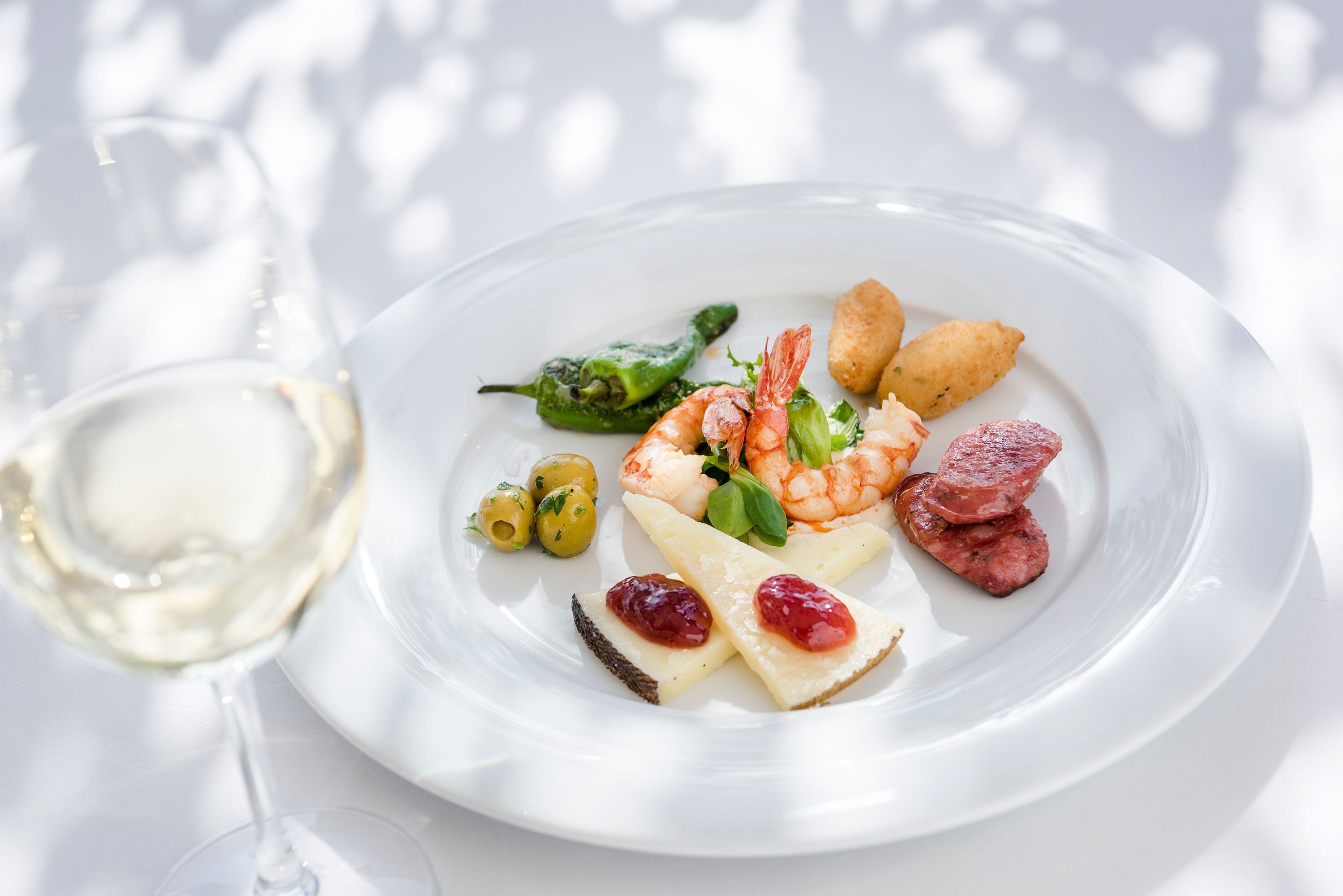 A white plate with shrimp, cheese, olives, and a glass of white wine.