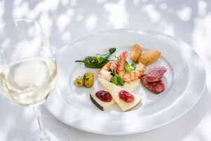 A white plate with shrimp, cheese, olives, and a glass of white wine.