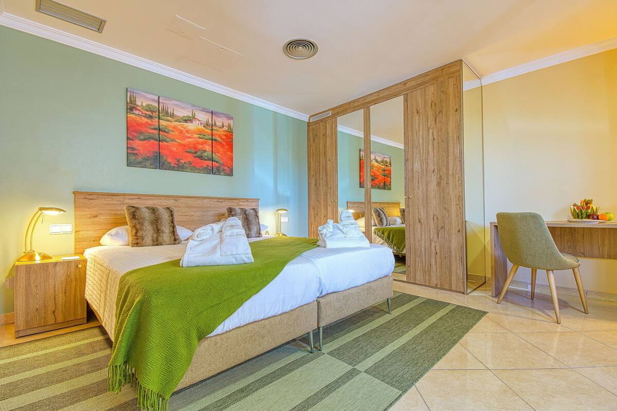 Una habitación de hotel con cama, mesita de noche, una silla, escritorio y espejo.