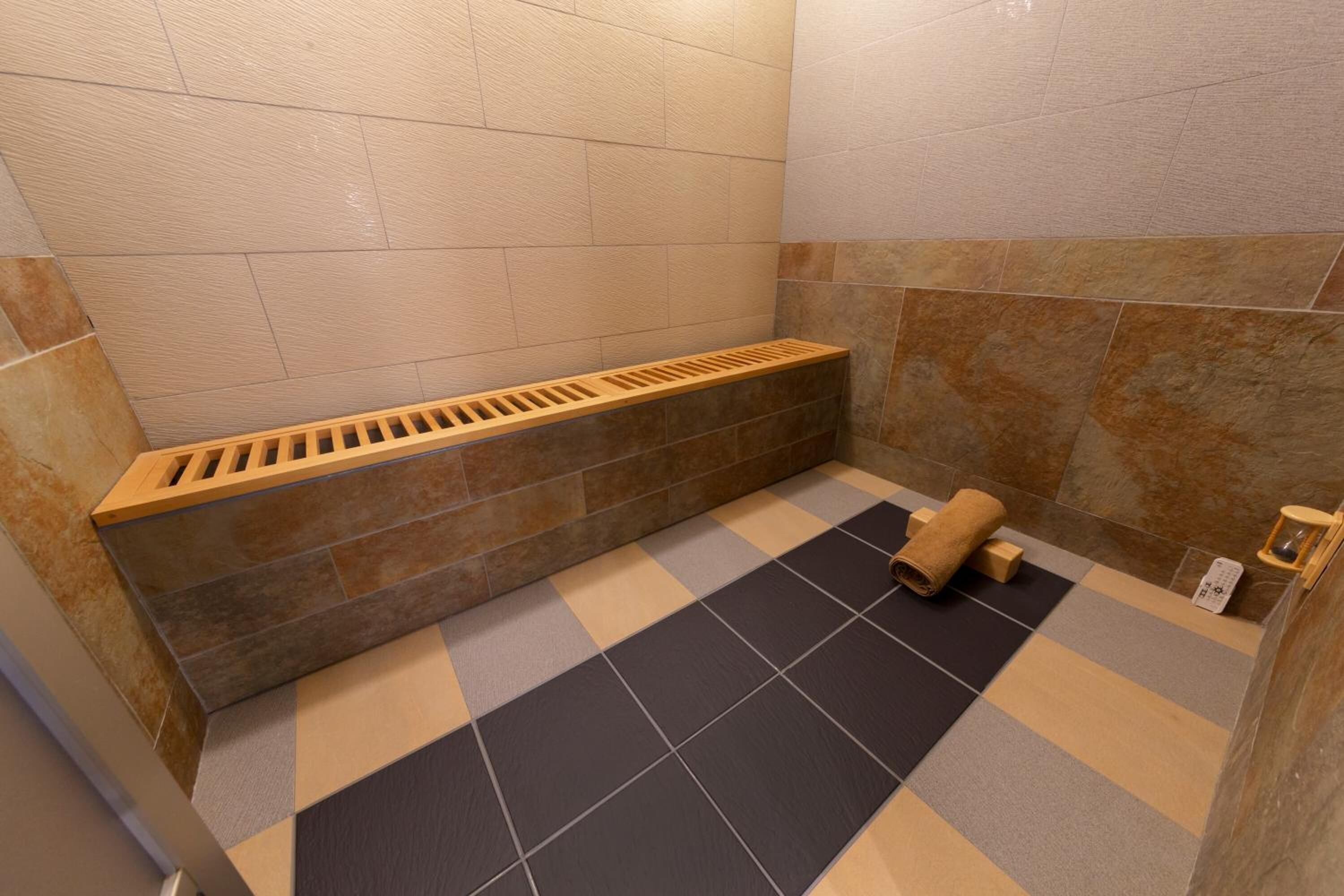 A bathroom with a checkered floor, a wooden bench, and a towel on the floor.