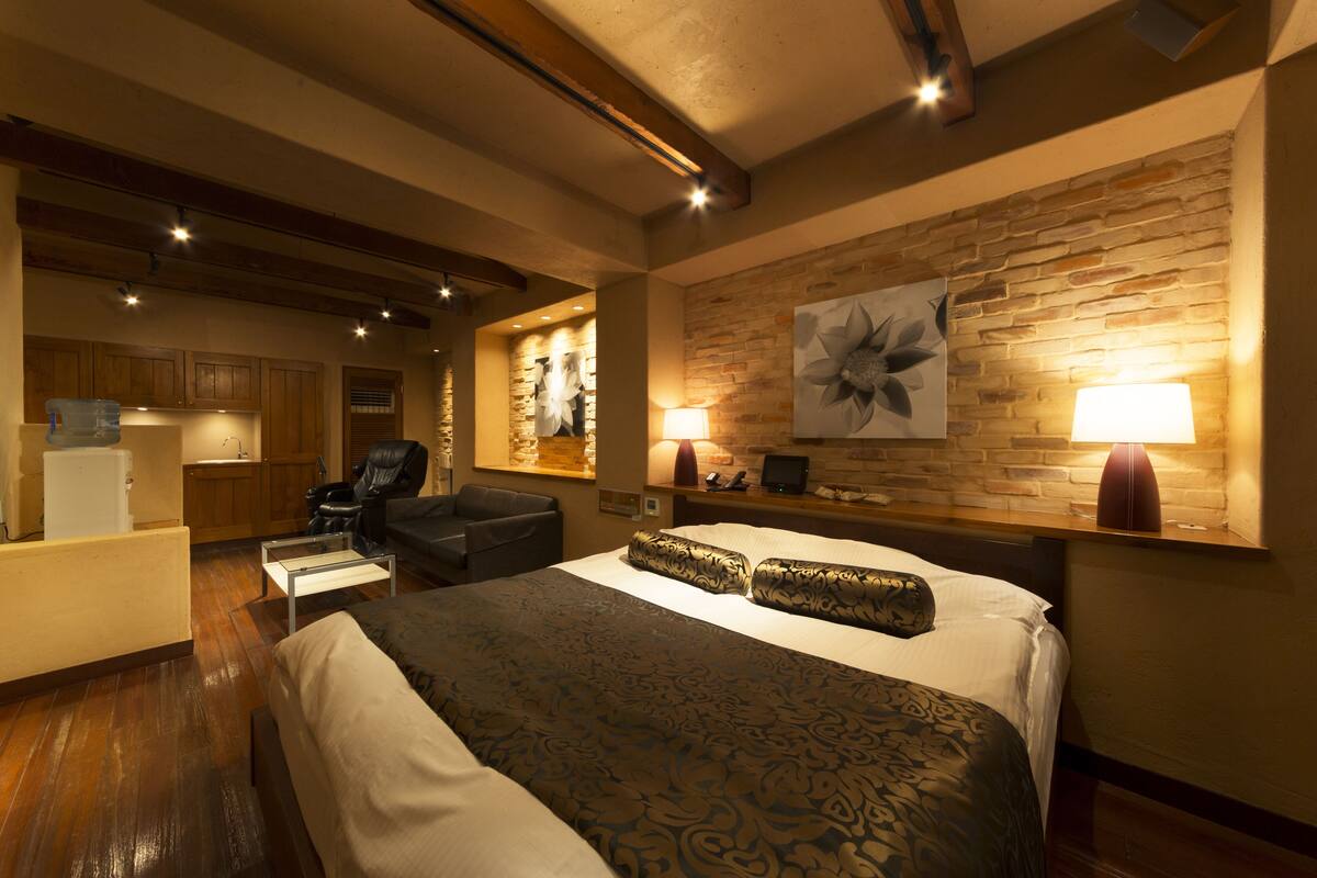 A hotel room with a large bed, a desk, a chair, a sofa, a fireplace, and a stone wall.