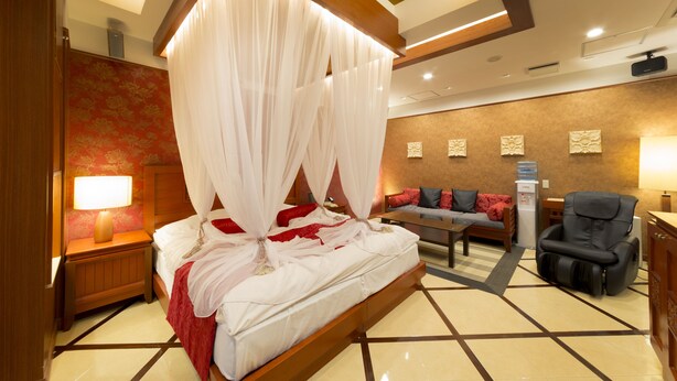 A bedroom with a canopy bed, a sofa, a massage chair, and a small table. - Hotel Lotus Nara - Adults Only (Nara)