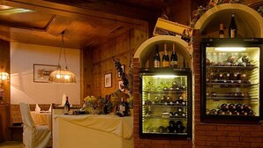 A cozy room with a dining table, chairs, and a red carpet. There are wine racks with bottles and a hanging light fixture. - Hotel Tia Apart (Kaunertal)