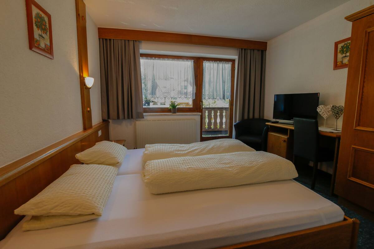 A hotel room with two beds, a desk with a computer, a TV, and a window with curtains.