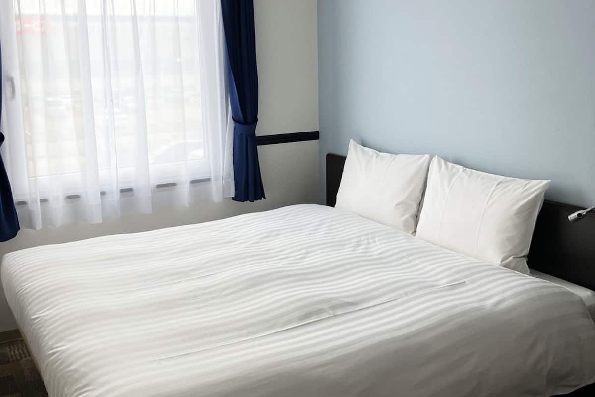 Une chambre d’hôtel avec un grand lit, une tête de lit et une fenêtre avec des rideaux.