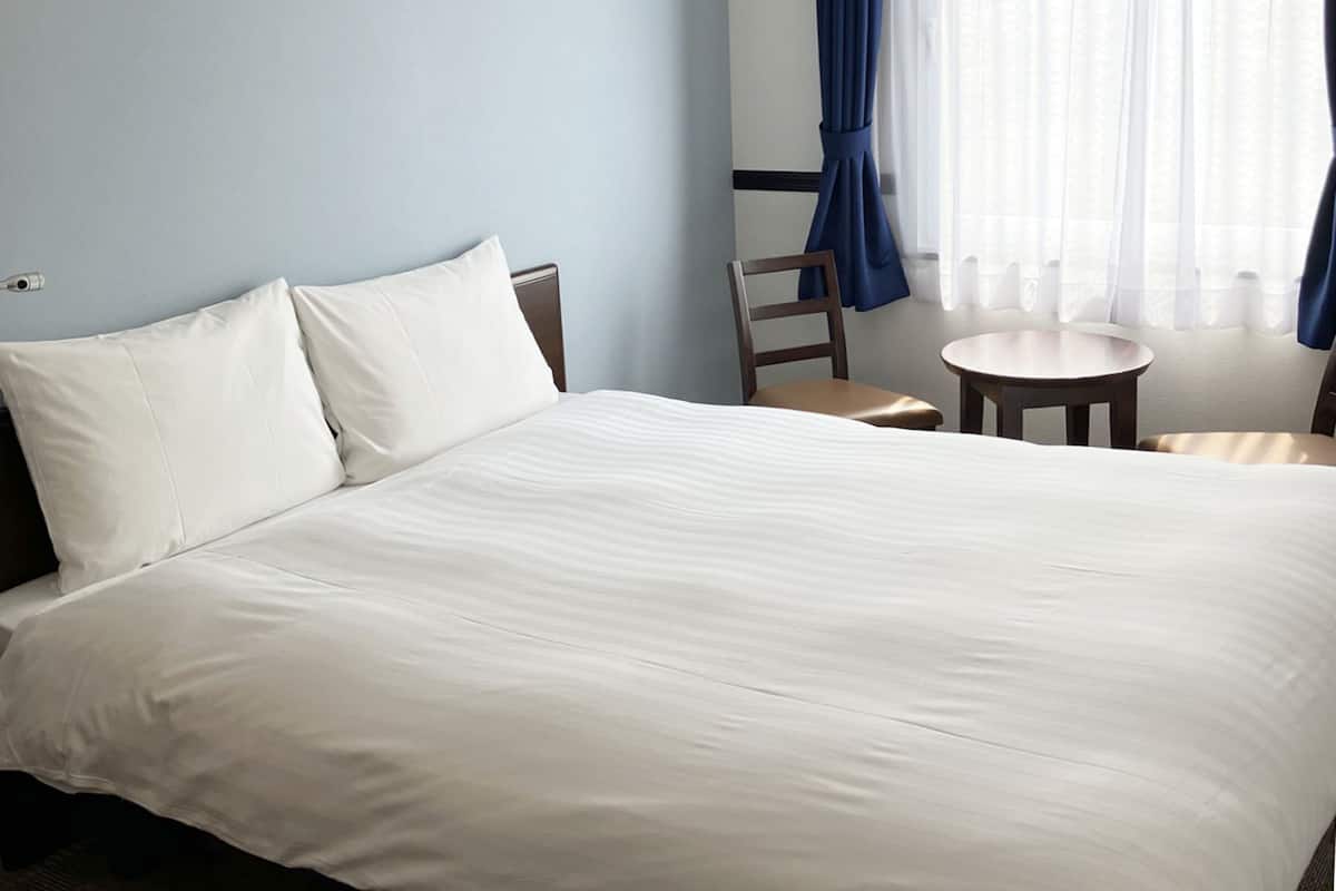 Une chambre d’hôtel avec un grand lit, une chaise, une petite table et une fenêtre avec des rideaux.